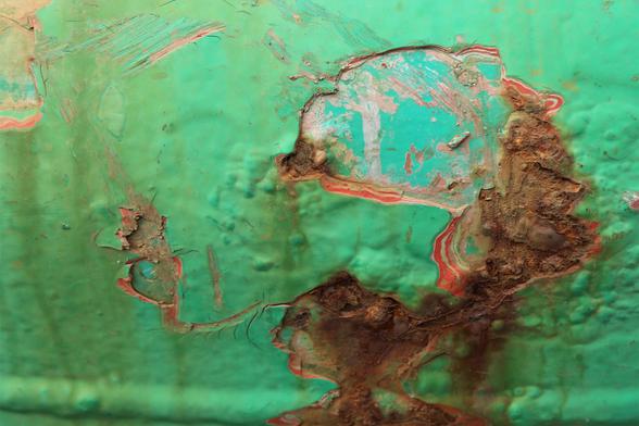 bright green / blue paint eroded away  to reveal lines of previous paint jobs and rusting. Weathering has developed thick blotches of paint as well as scratches.