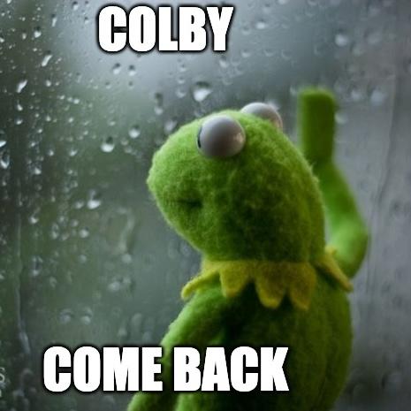 A green Kermit the Frog toy looking out a rainy window with the words COLBY COME BACK