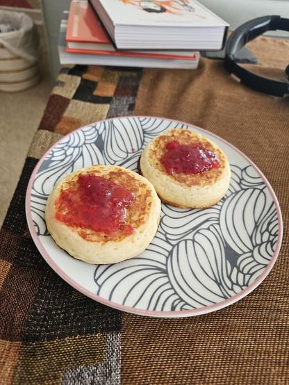 A photo of two jammed crumpets on a plate with books in the background.
