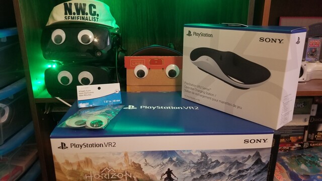 PlayStation VR 2 with charging stand in box, sitting in front of a Valve Index, Oculus Rift S, and Nintendo Labo, all with googly eyes on them. A pack of unused googly eyes is also visible because they are required modifications to any and all VR headsets.