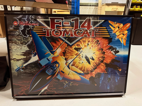 F-14 Tomcat's backglass out of the game. It has a picture of a scene where a fighter jet is flying towards the player, with an enemy jet exploding in the background. 