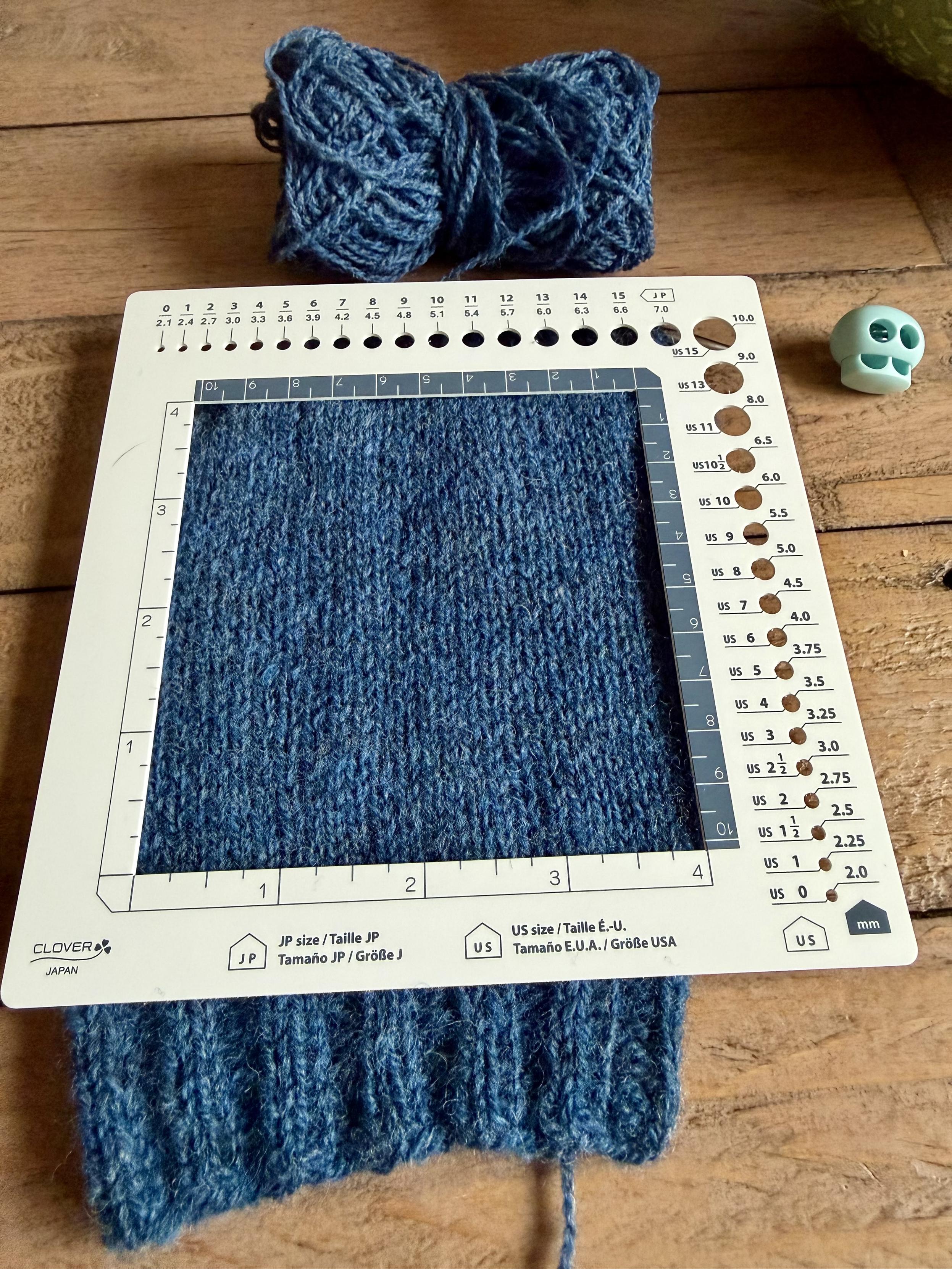 Blue stockinette stitch sleeve in a 10 cm by 10 cm gauge square measuring thing.