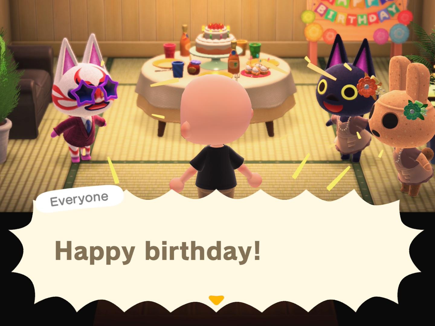 Animal Crossing: New Horizons screenshot. Set in Kabuki's house, with Kabuki, Kiki, and Coco all dressed up and yellowing "Happy Birthday" to a bald, light skinned human who is walking into the room. A table with a cake is set up in the middle of the room and a large Happy Birthday banner is in the upper right-hand corner.