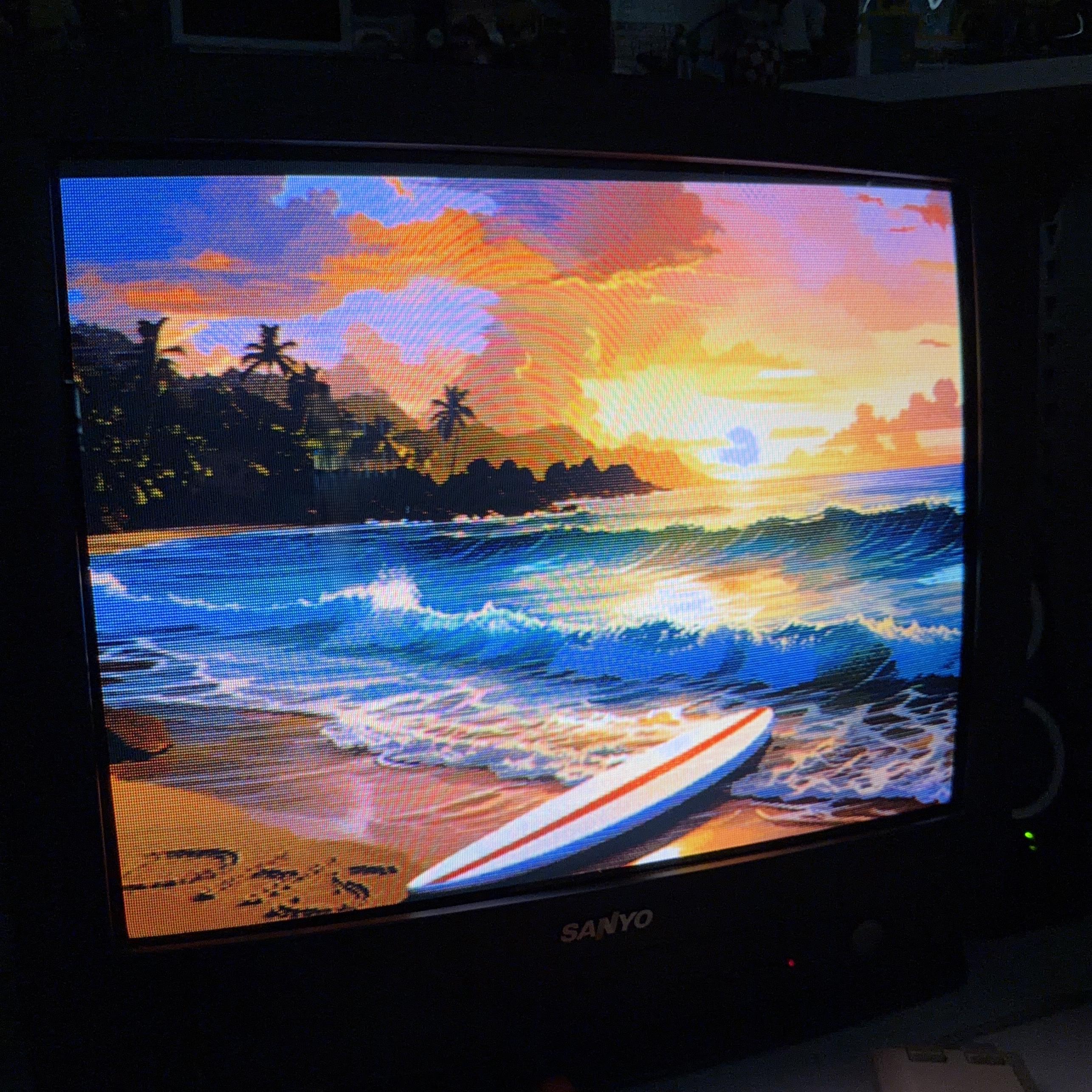 A vivid tropical beach sunset displayed on a vintage Sanyo CRT television. The screen shows golden sunlight reflecting off rolling waves, with a surfboard resting on the wet sand in the foreground. Palm trees and rocky cliffs silhouette against a sky painted in warm orange, pink, and purple hues.