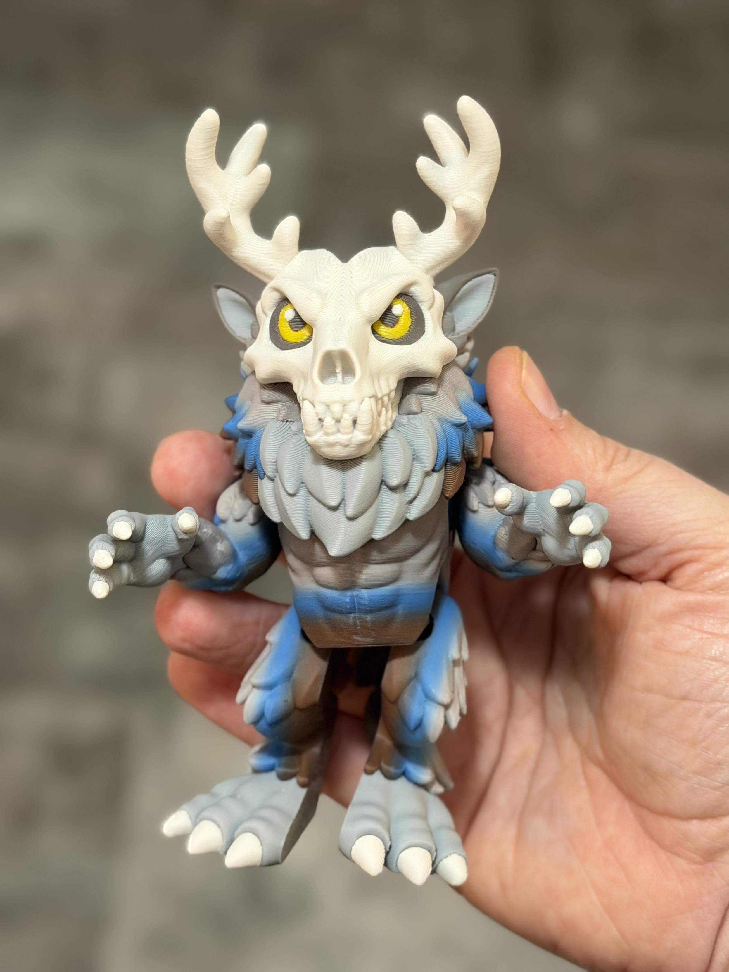 Hand holding a small figure of a wendigo. The eyes are yellow, with a bone white skull and blue grey and brown body.