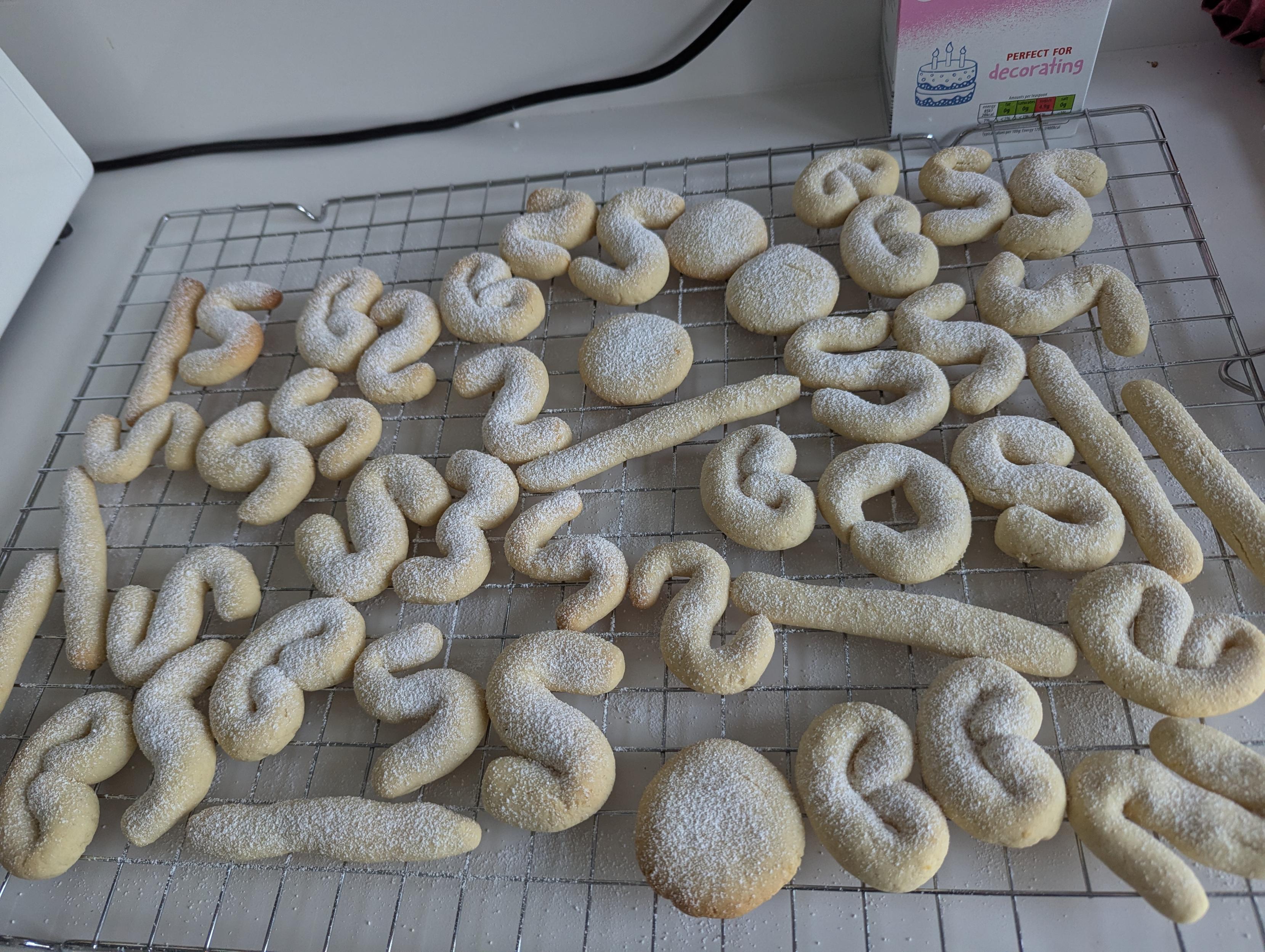 Tens of squiggly cookies dusted with icing sugar on a wire rack